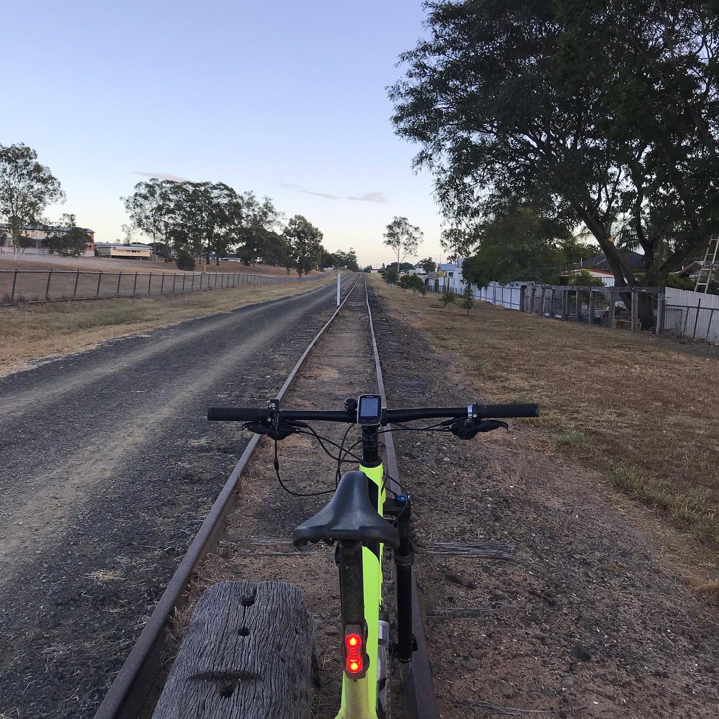 Bicycle stopped on old railway tracks beside a dirt road, with trees and fences lining the path at dusk.