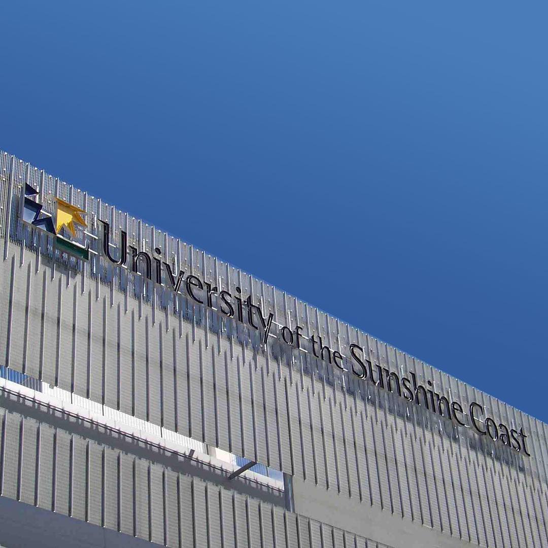 University of the Sunshine Coast sign on a modern silver building beneath a clear blue sky.