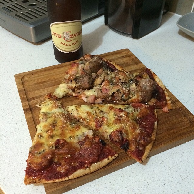 Two slices of homemade pizza on a wooden board beside a bottle of Little Creatures Pale Ale on a kitchen counter.