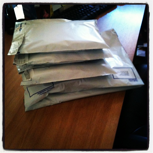 Stack of five padded mailing envelopes on a wooden desk.