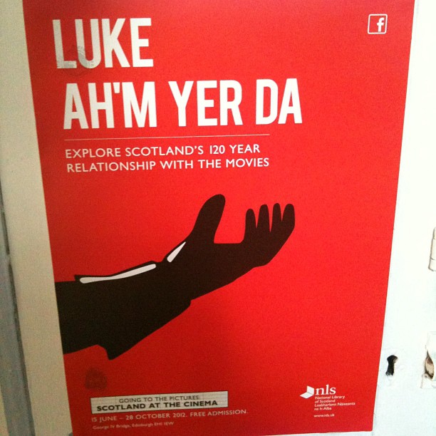 Red poster with white text reading “LUKE AH'M YER DA” and “Explore Scotland’s 120 year relationship with the movies,” plus a black outstretched hand.