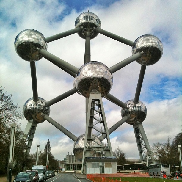 Large metallic spheres connected by thick tubes in a geometric structure above a street under a cloudy sky.