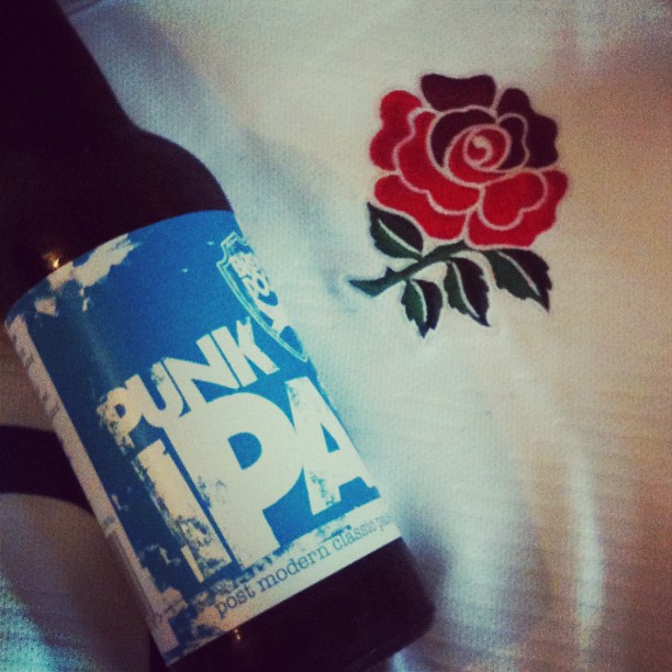 Bottle labeled "PUNK IPA" lying on white fabric with a red rose embroidery.