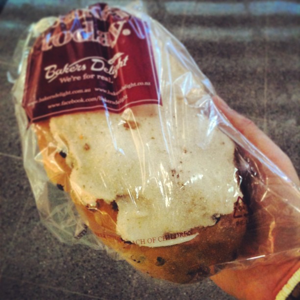 Hand holding a partially sliced loaf of raisin bread in clear plastic packaging with a maroon label.
