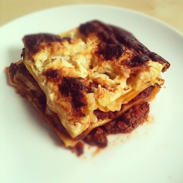 Slice of lasagna with browned melted cheese on a white plate.