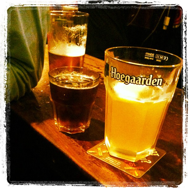 Three glasses of beer on a wooden table, including a Hoegaarden pint in the foreground.