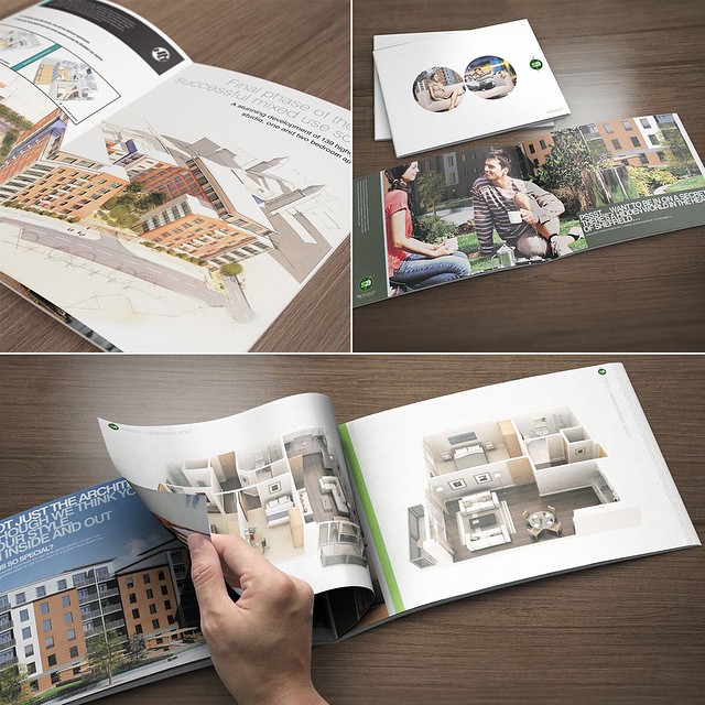 Open architectural brochure and booklet on a wooden table, with building renderings, floor plans, and a hand turning a page.