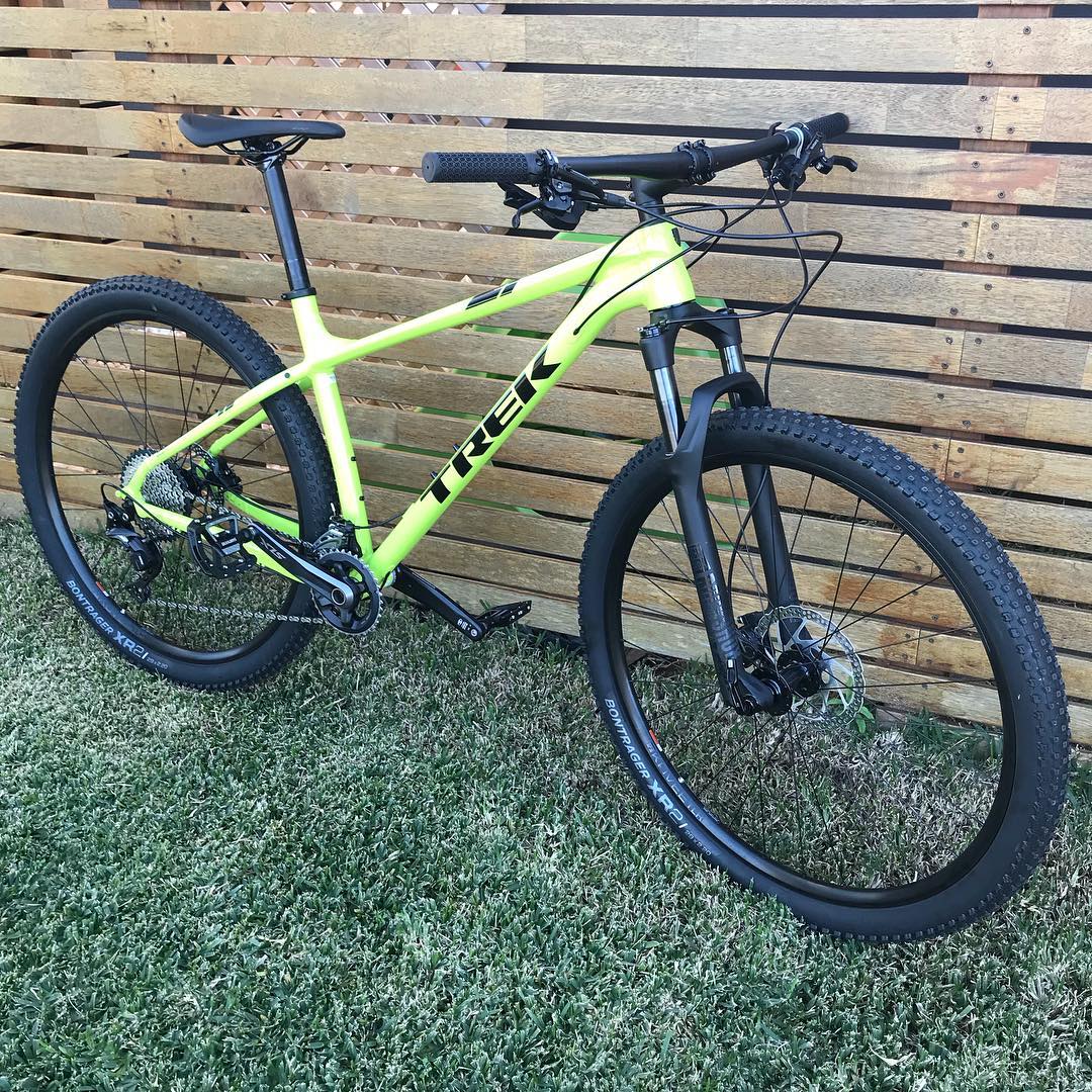 Neon green Trek mountain bike with black tires and front suspension leaning against a wooden slat fence on grass.