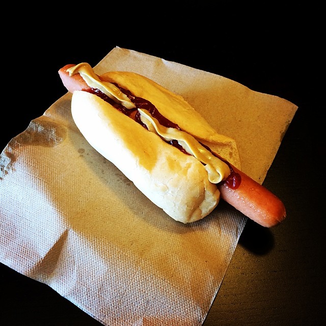 Hot dog in a bun with ketchup and mustard, resting on a folded napkin against a black background.