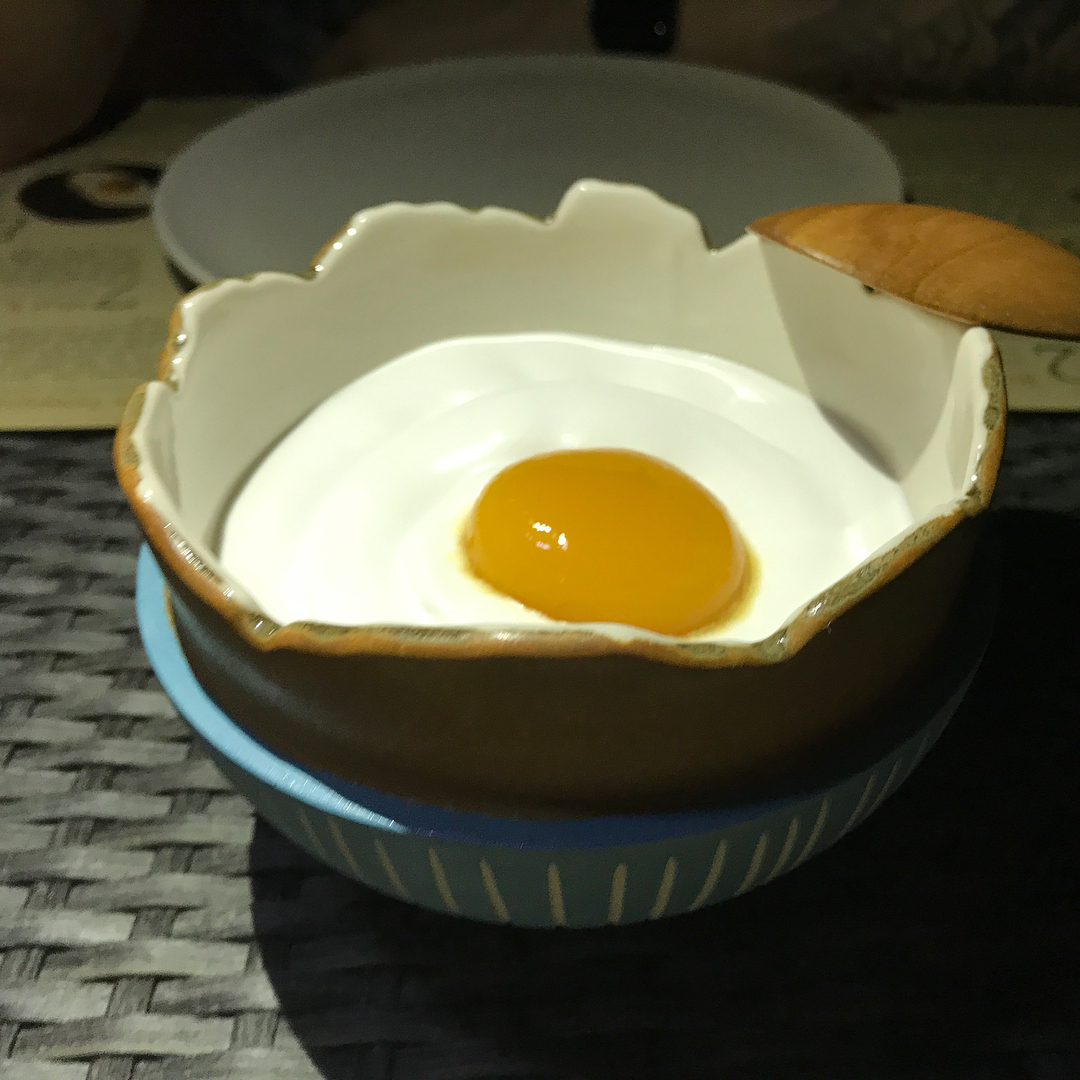 Raw egg yolk in a scalloped ceramic bowl with a wooden spoon resting on the rim, stacked on a blue bowl.