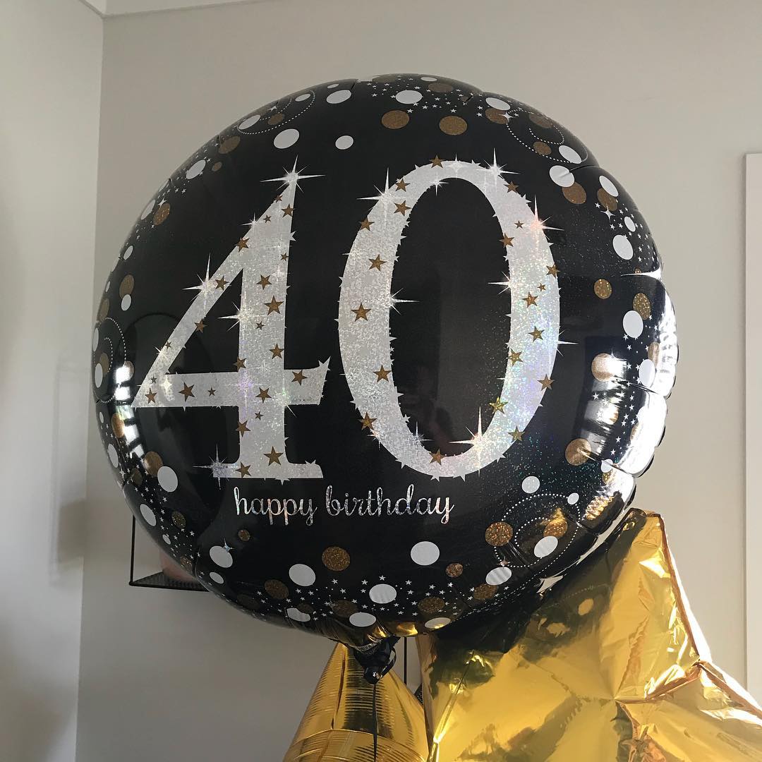 Black birthday balloon with glittery silver 40, white and gold dots, and “happy birthday” text, with gold balloons below.