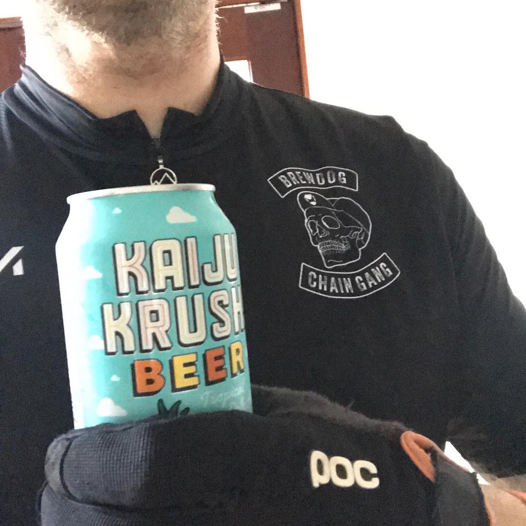 Person in a black cycling jersey and glove holding a can labeled "Kaiju Krush Beer.