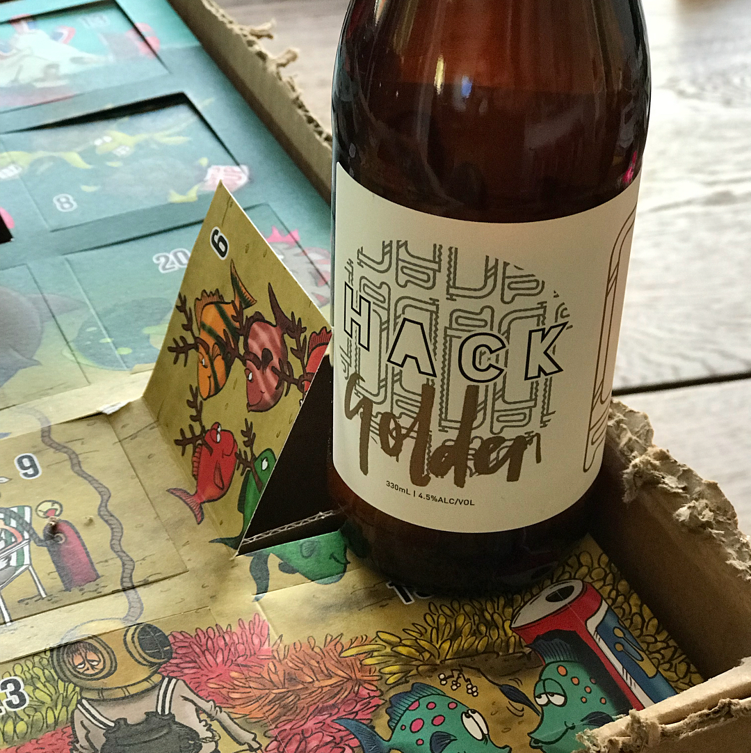 Brown beer bottle labeled “BLACK” standing in a cardboard tray beside a folded card on a colorful illustrated game board.