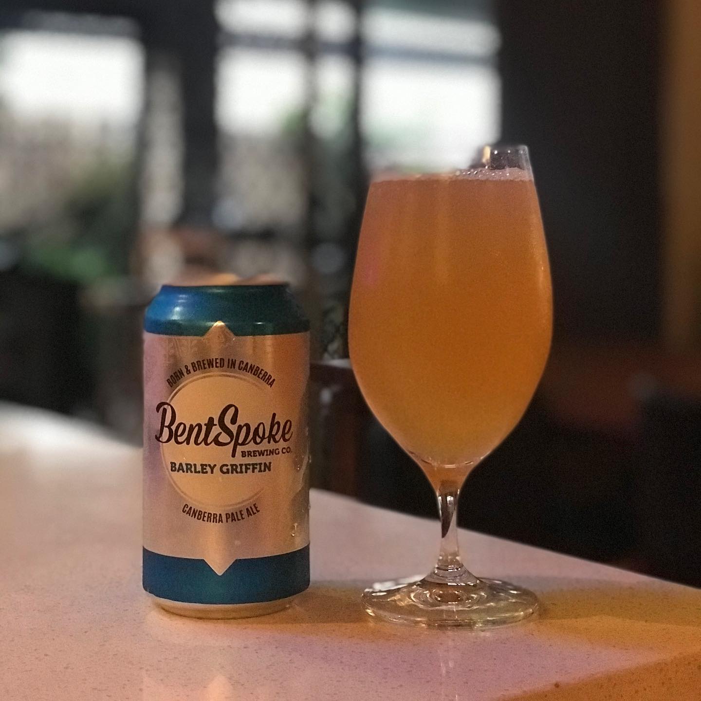 Can of BentSpoke Barley Griffin pale ale beside a stemmed glass of hazy golden beer on a countertop.
