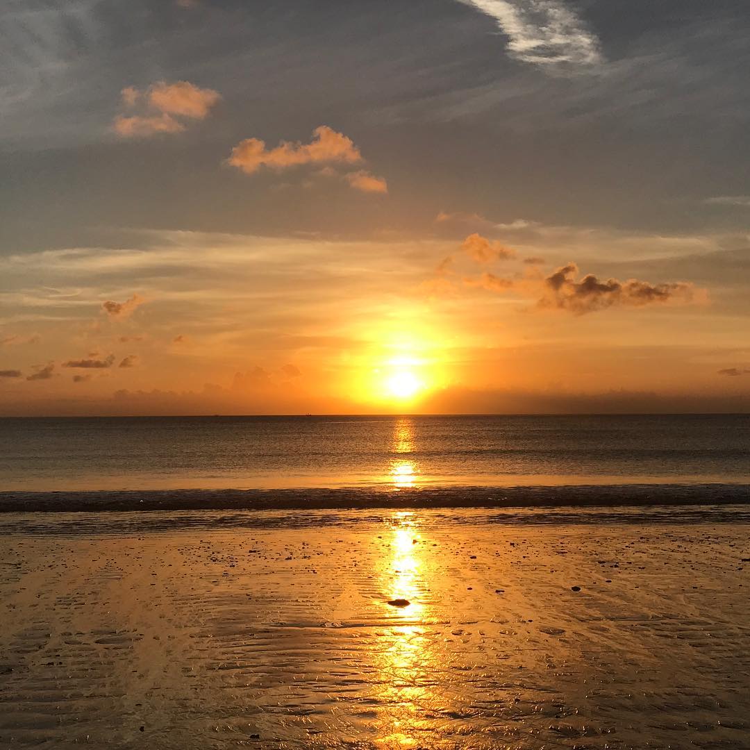 Golden sunset over a calm ocean, with scattered clouds and bright reflections stretching across wet sand.