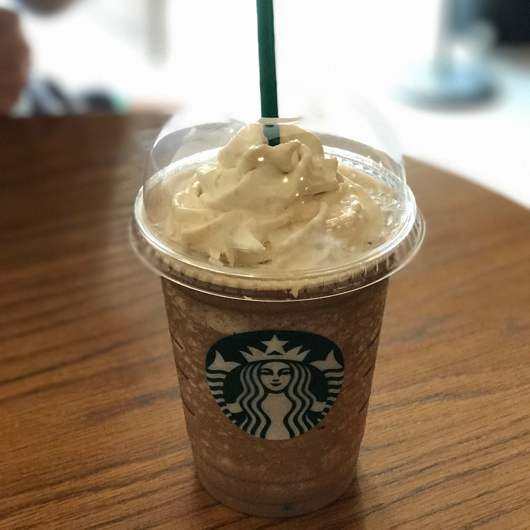 Starbucks blended drink topped with whipped cream in a clear plastic cup on a wooden table.