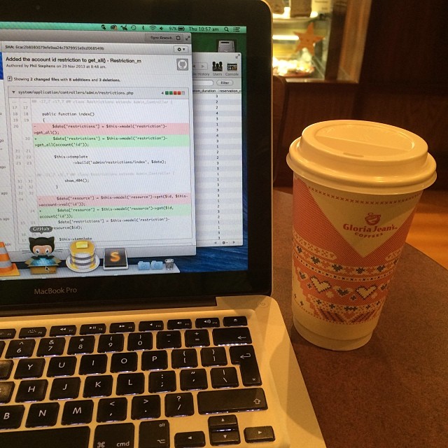 MacBook Pro displaying code beside a patterned Gloria Jean's Coffee takeaway cup on a wooden table.