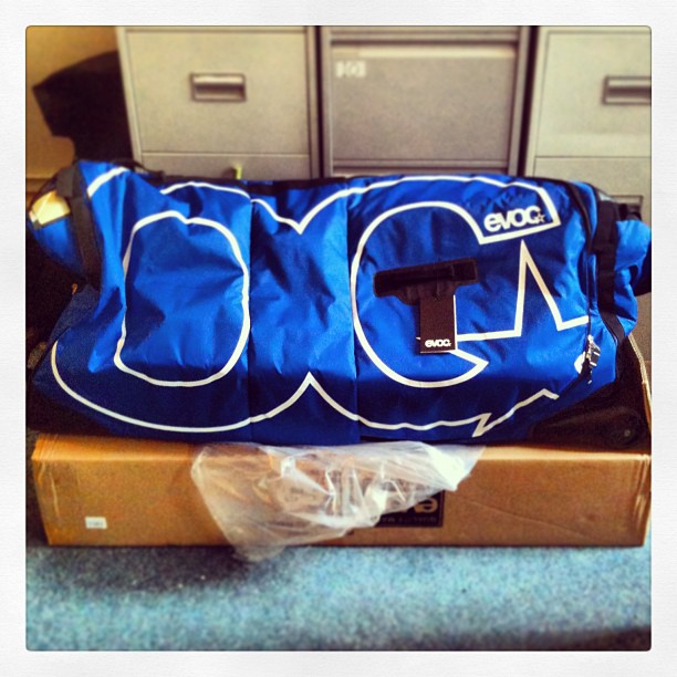 Blue EVOC duffel bag resting on a cardboard box in front of metal filing cabinets.