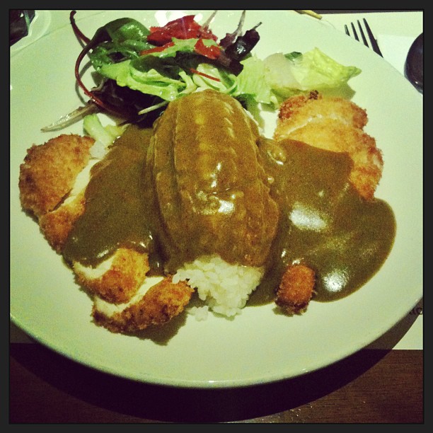Plate of rice topped with curry sauce and breaded cutlets, with a mixed green salad on the side.
