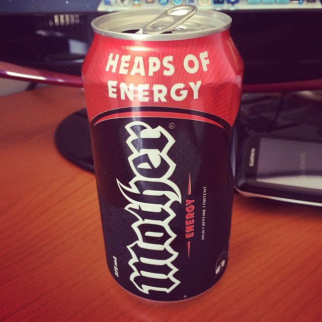 Opened Mother Energy drink can on a desk beside a phone and computer monitor.