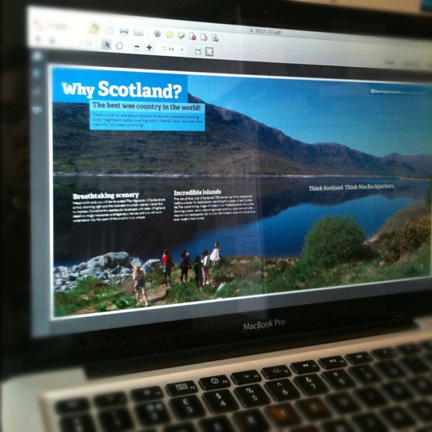 Laptop screen showing a PDF titled “Why Scotland?” with a scenic landscape and people hiking, above a blurred keyboard.