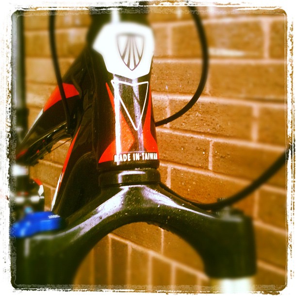 Close-up of a bicycle head tube and front fork with black cables against a brick wall.