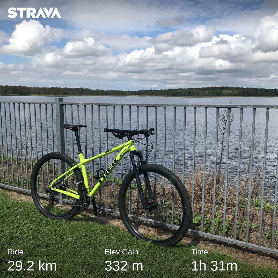 Neon yellow mountain bike beside a metal fence by a lake under a cloudy sky, with Strava ride stats overlaid at the bottom.
