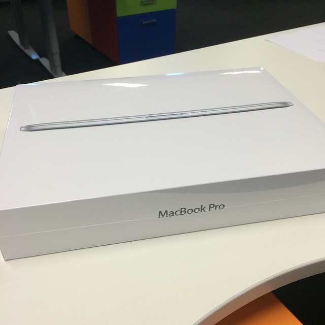 White MacBook Pro box on a desk with the laptop pictured on the lid.