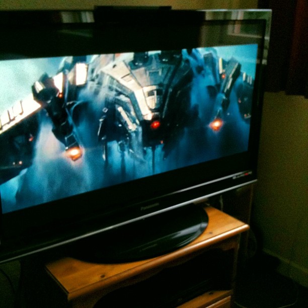 Television on a wooden stand displaying a sci-fi spacecraft scene with glowing lights and blue smoke.