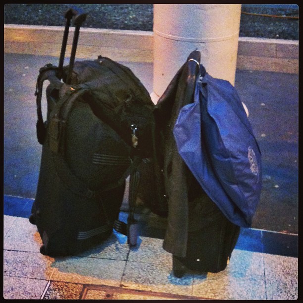 Two rolling suitcases stand beside a pole, with a blue bag draped over one handle.