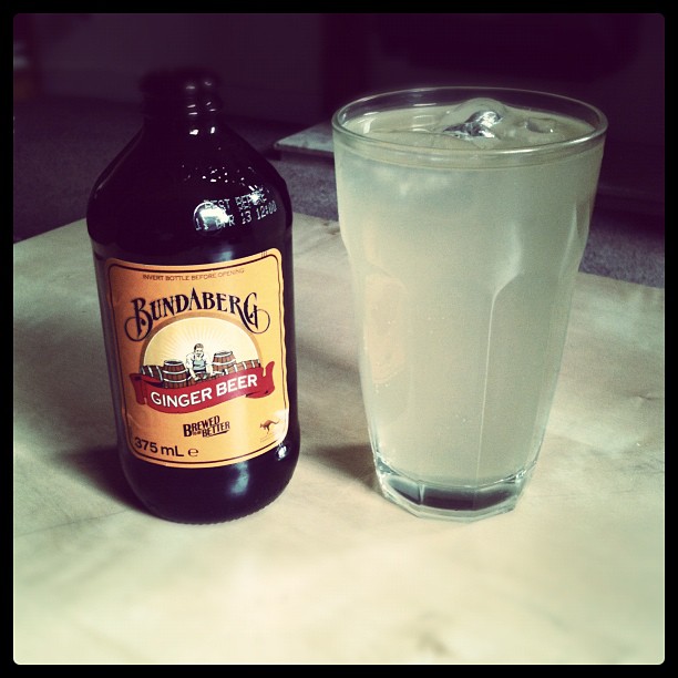 Bottle of Bundaberg ginger beer beside a glass of pale iced drink on a marble surface.