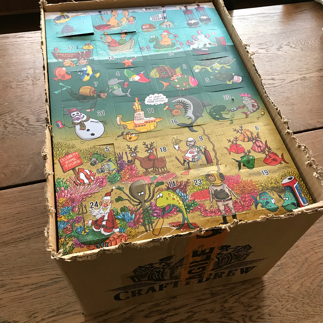 Open cardboard box holding a colorful underwater-themed advent calendar with numbered doors and cartoon sea creatures on a wooden table.