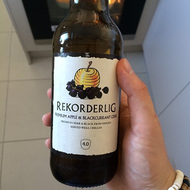 Hand holding a Rekorderlig premium apple and blackcurrant cider bottle indoors.
