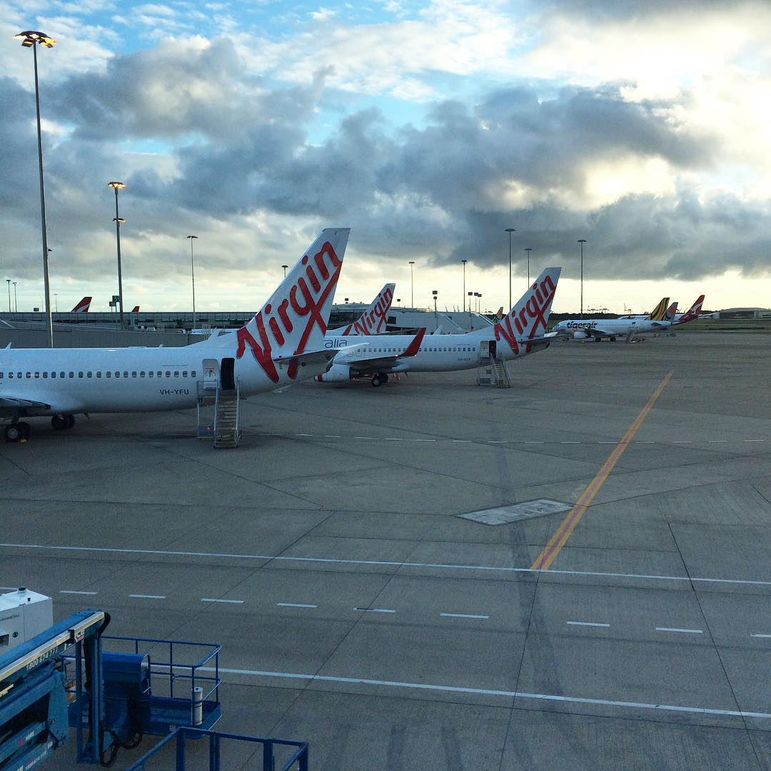 Several Virgin airplanes parked on an airport tarmac under a cloudy sky.