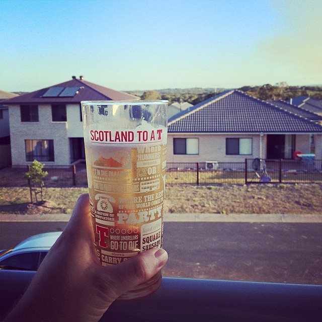 Hand holding a clear printed glass against a suburban street view with houses and a blue sky.