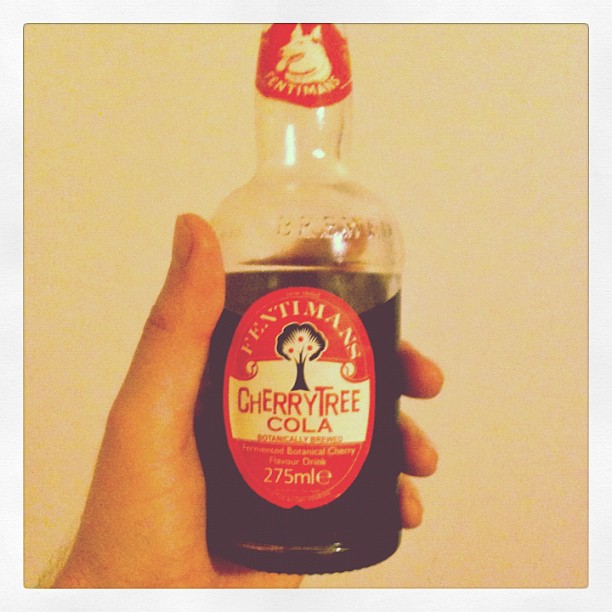 Hand holding a bottle of Fentimans Cherry Tree Cola against a plain light background.