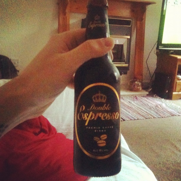Hand holding a bottle labeled Double Espresso in a living room with a fireplace and TV in the background.