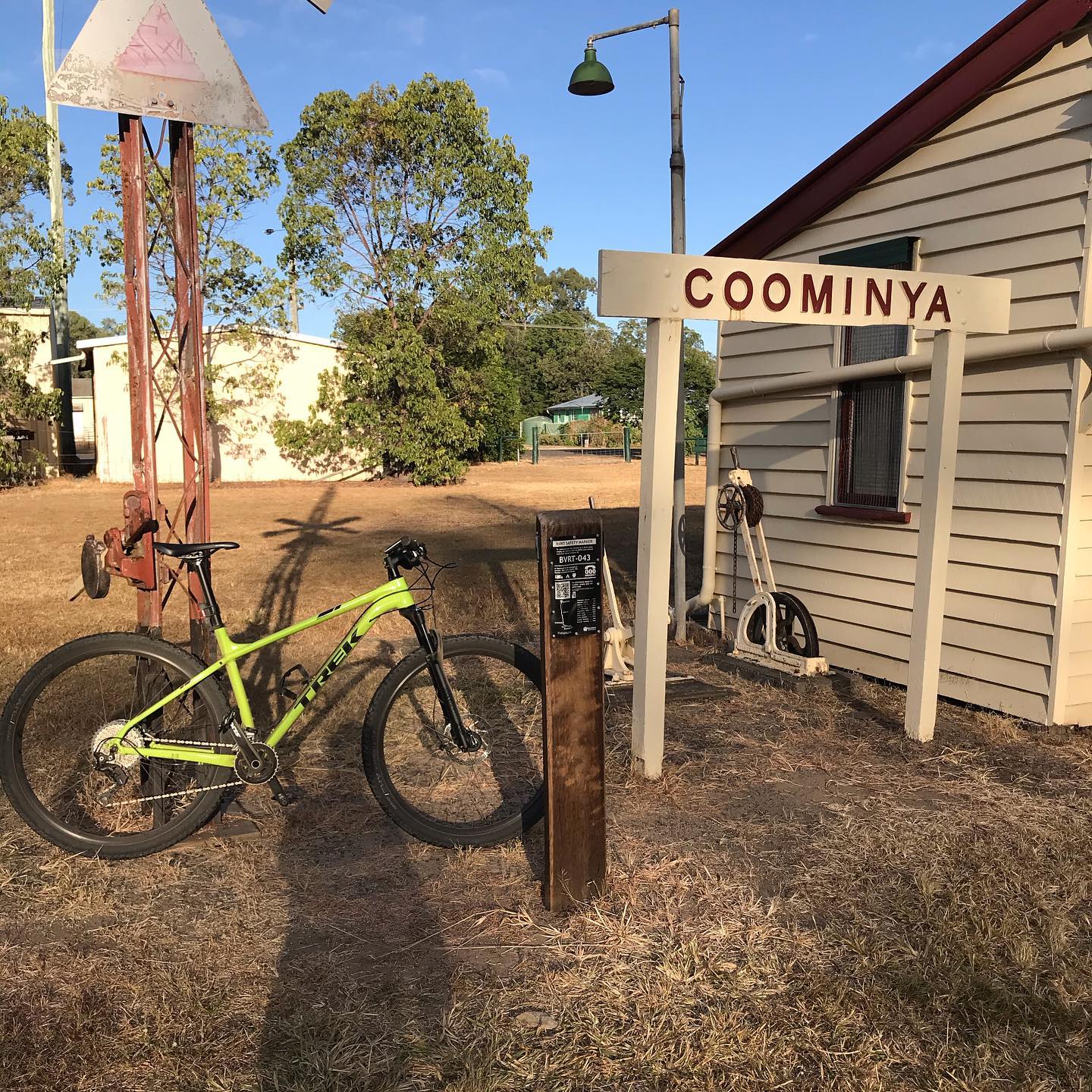 Bright green bicycle beside a Coominya station sign and old railway equipment next to a weatherboard building.