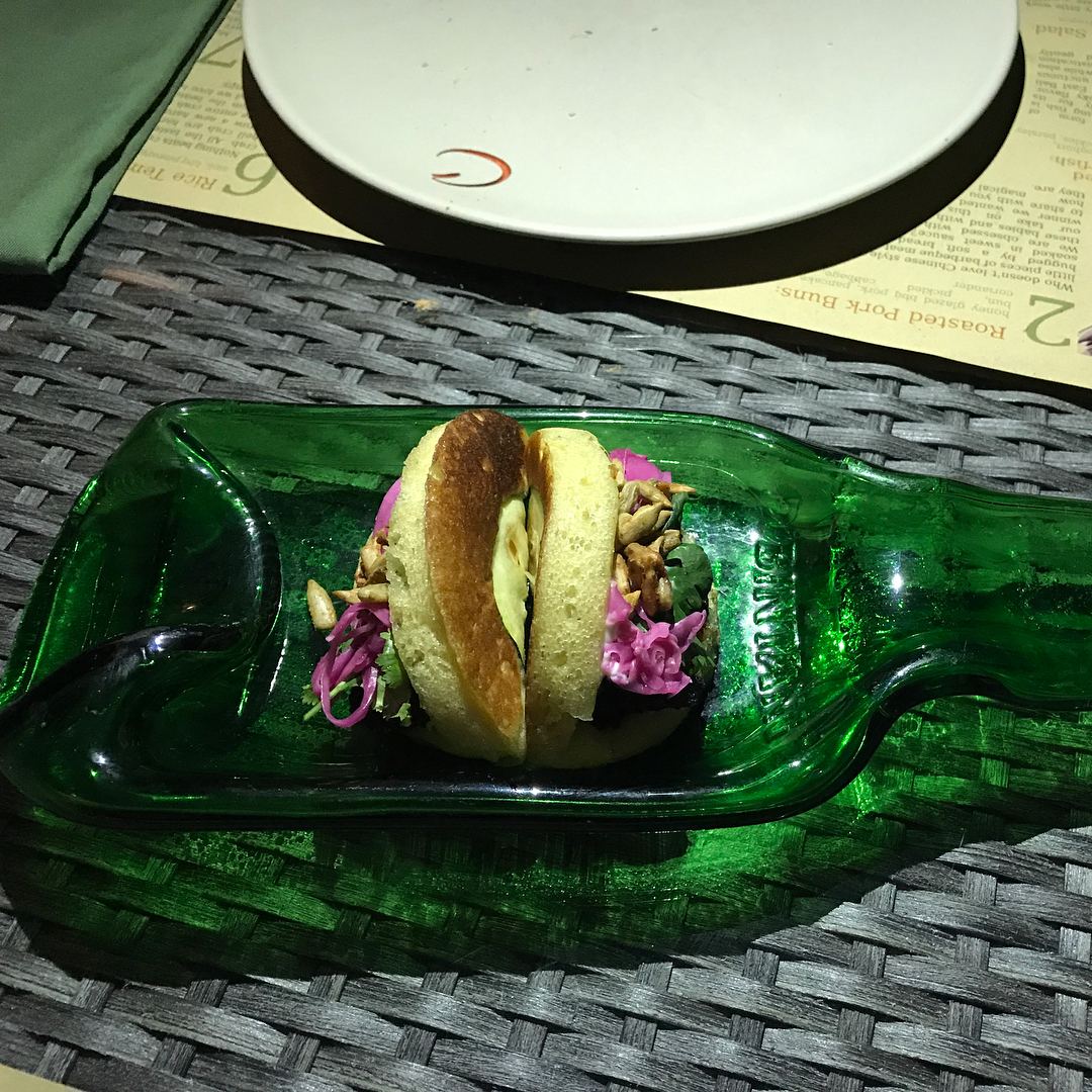 Small sandwich with purple cabbage and nuts served in a green glass bottle-shaped dish on a woven placemat.