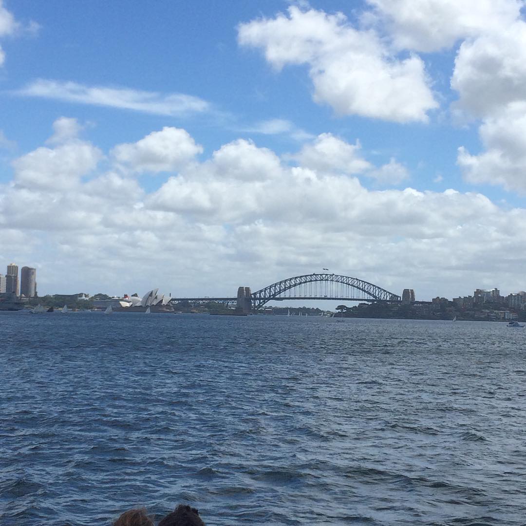 Sydney Harbour Bridge and the Sydney Opera House across blue water under a sky filled with scattered clouds.
