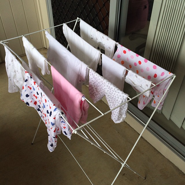 Baby clothes and cloths hanging on a white drying rack on a patio beside a sliding glass door.