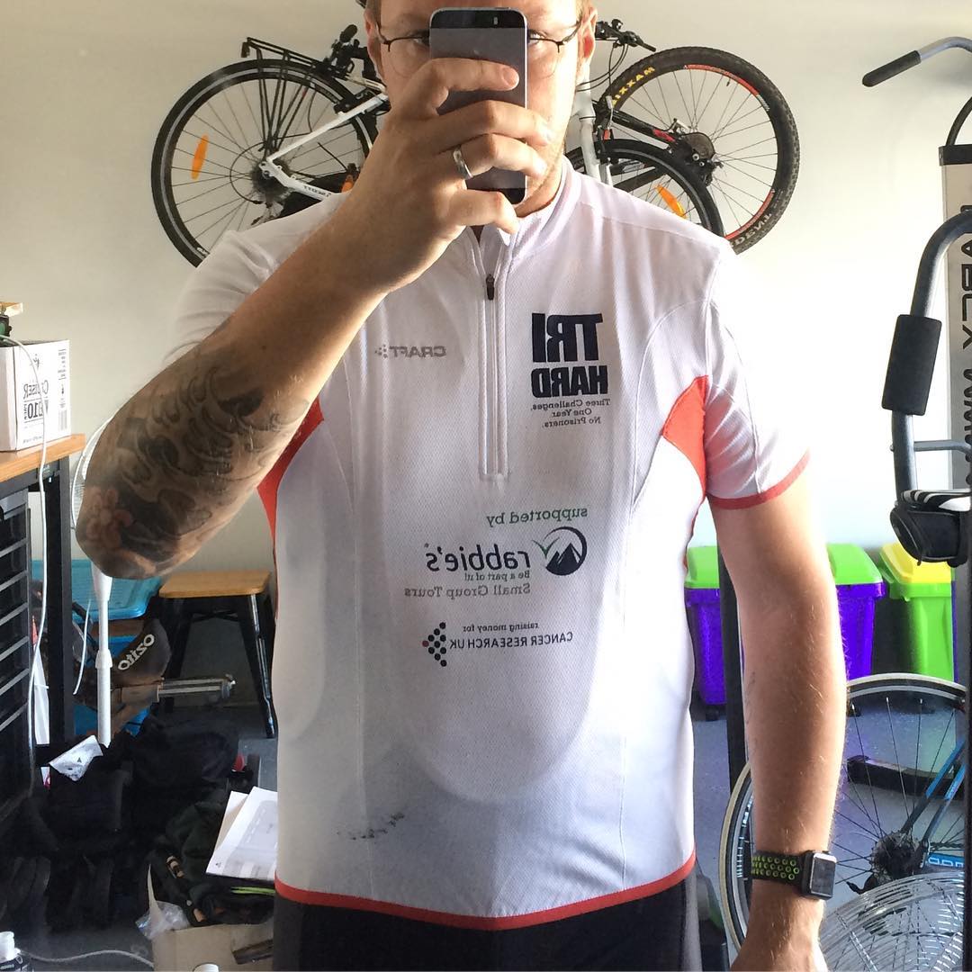 Person taking a mirror selfie in a white cycling jersey, with bikes hanging on the wall and exercise equipment in the room.