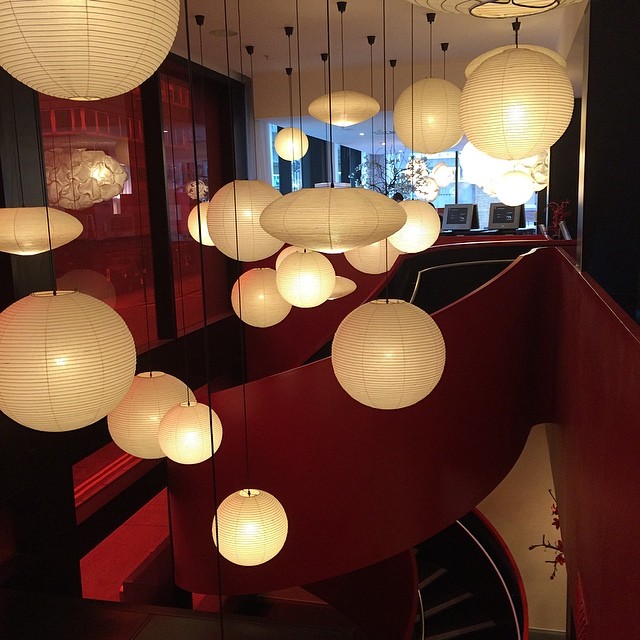 White paper lantern pendant lights hang above a curved red staircase in a modern interior.