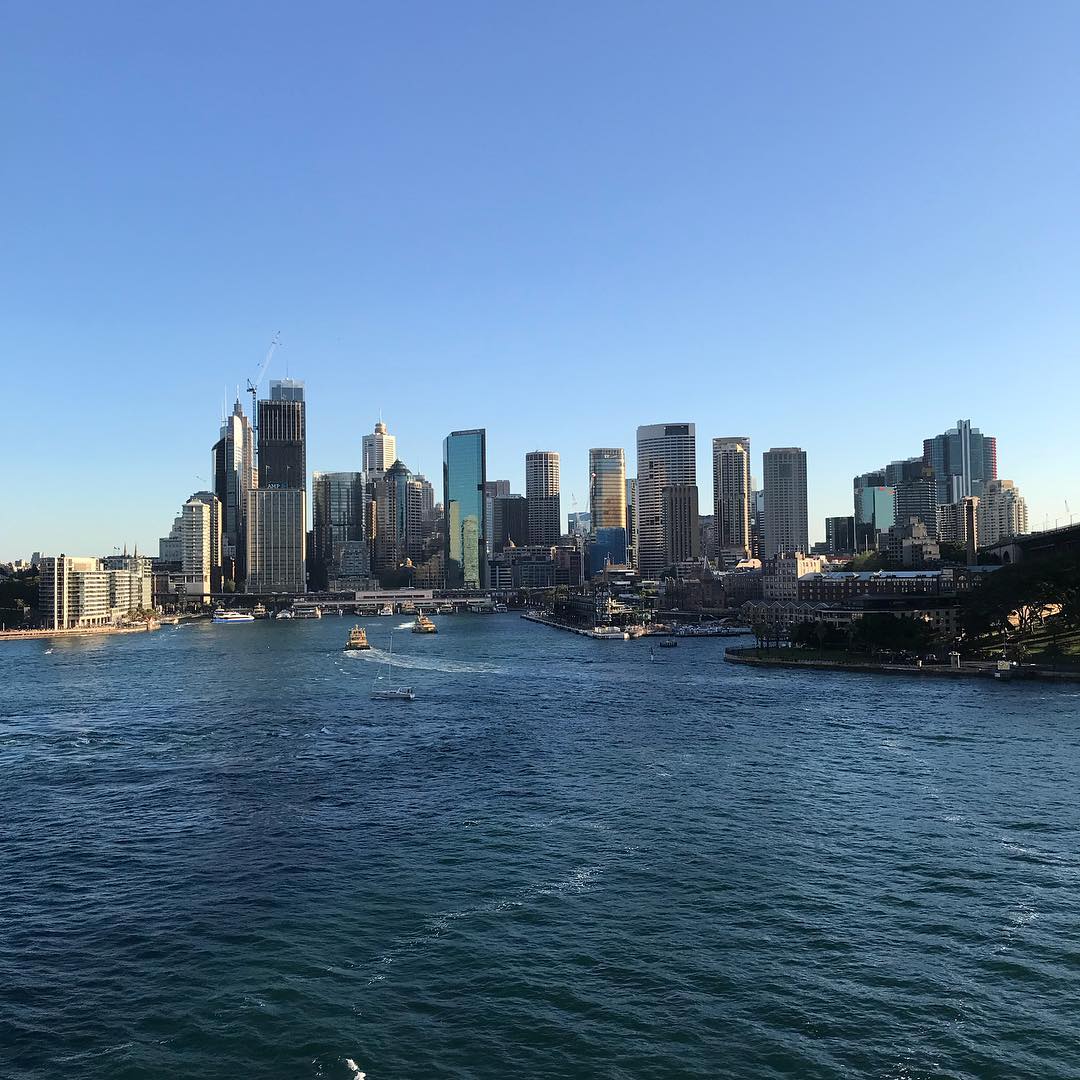 City skyline along a harbor with several boats on blue water under a clear sky.