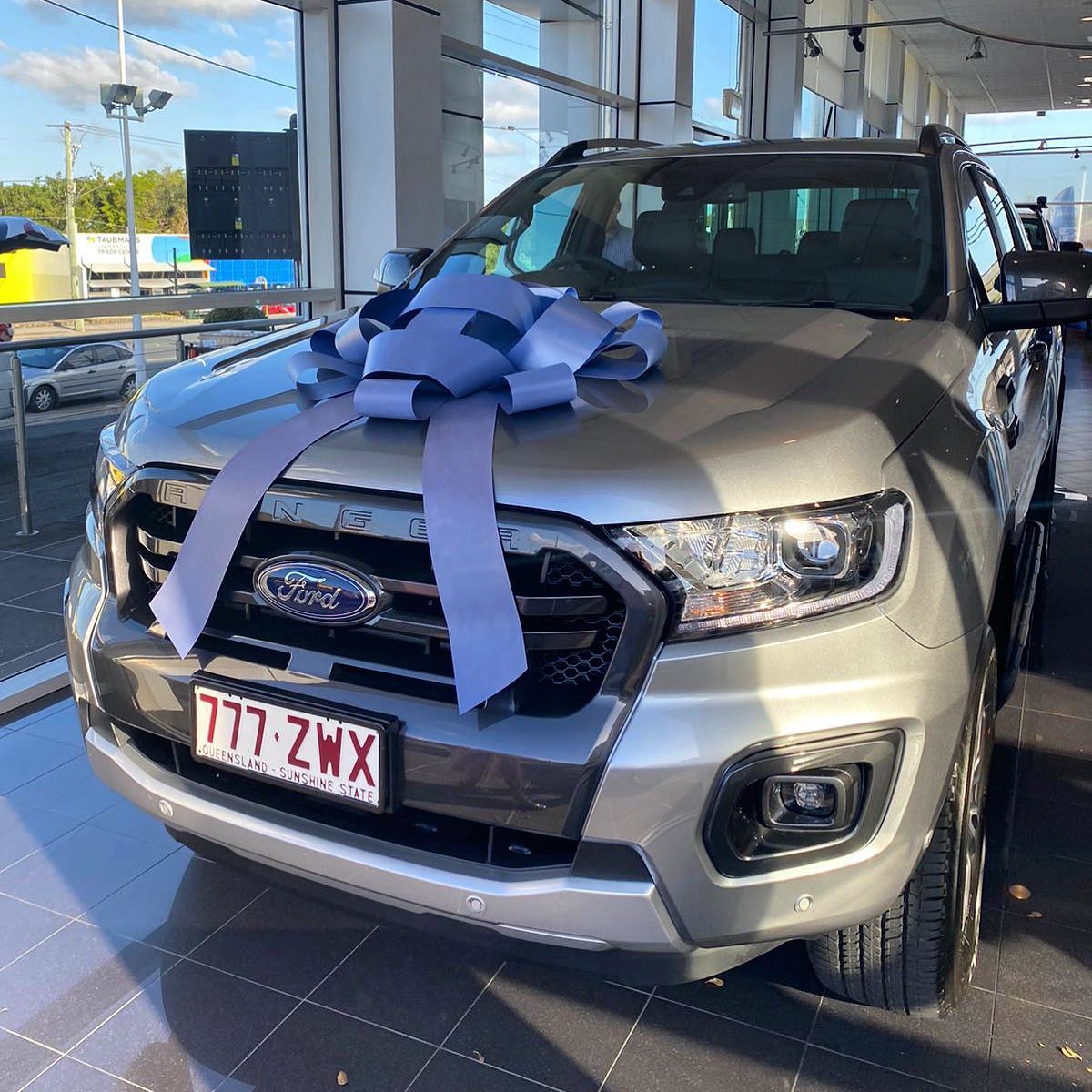Silver Ford Ranger in a showroom with a large blue bow on the hood.