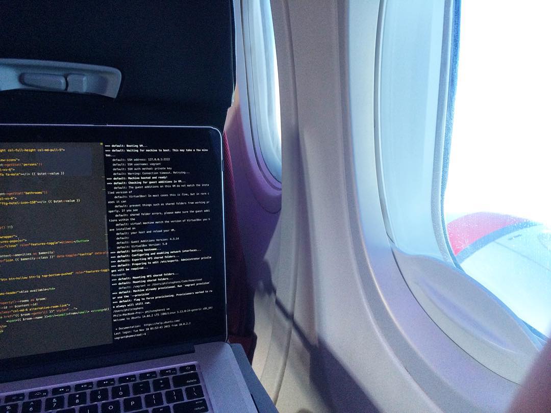 Laptop displaying code and terminal text beside an airplane window with bright daylight outside.