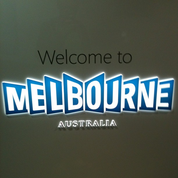 Sign reading “Welcome to Melbourne Australia” with Melbourne in large blue and white letters on a dark wall.