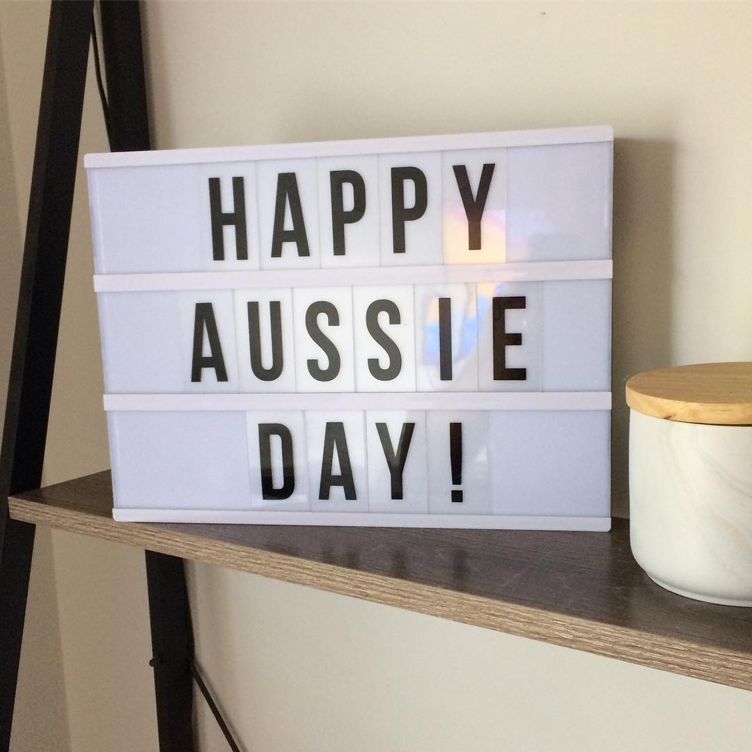 Lightbox sign on a shelf reading “HAPPY AUSSIE DAY!” next to a white jar with a wooden lid.