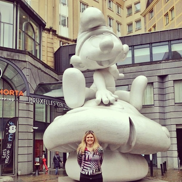 Woman standing in front of a giant white Smurf statue outside a building entrance.