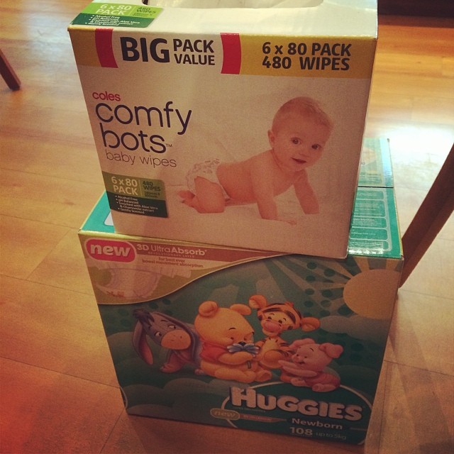 Two stacked boxes on a wooden floor: Coles Comfy Bots baby wipes on top of a Huggies Newborn diaper box.
